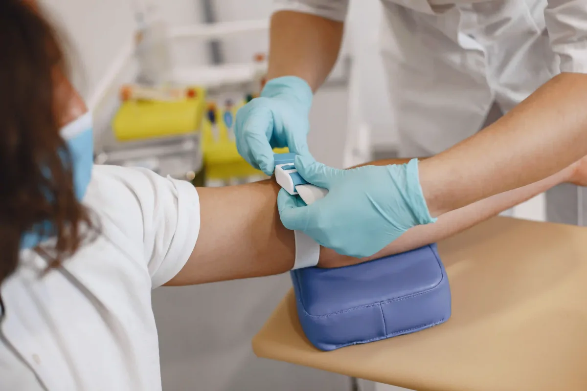 A phlebotomist in blue gloves preparing a patient's arm for a blood draw
